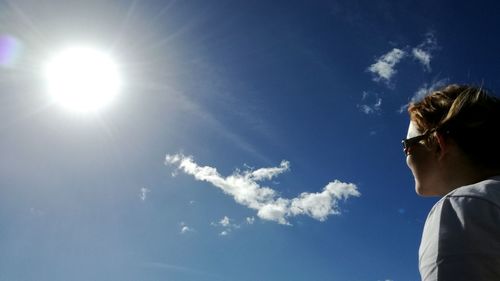 Low angle view of woman looking at sun in blue sky