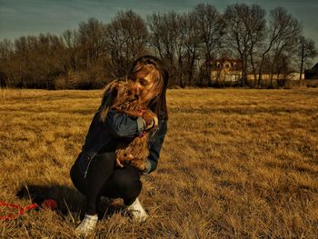 Full length of woman crouching while carrying dog on field