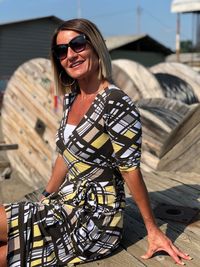 Portrait of smiling mature woman wearing sunglasses while sitting wooden spool