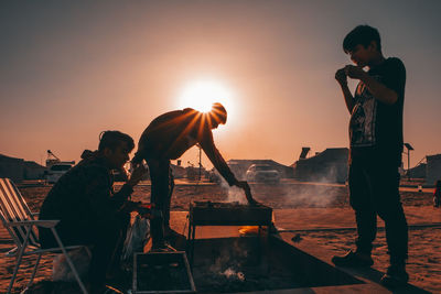 People standing on shore against sky during sunset