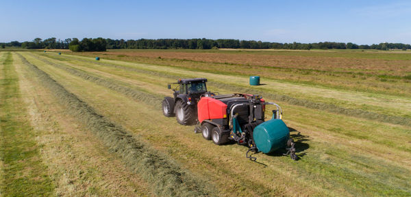 Black tractor with a red straw chamber press during the straw harvest on a mown field