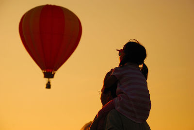 Father carrying daughter with hot air balloon against clear sky