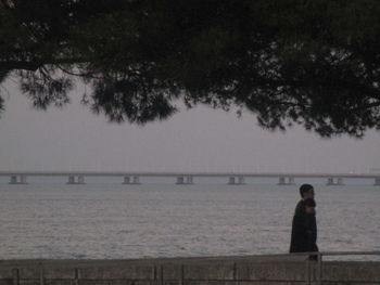 Rear view of silhouette man standing by sea against sky