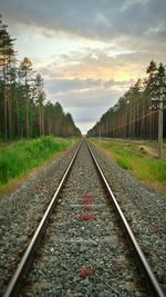 Railroad tracks on field against cloudy sky during sunset