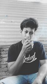 Portrait of young man looking away while sitting on wall