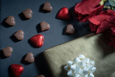 Closeup of heart-shaped chocolate confections, red roses, and a gift against a dark background.
