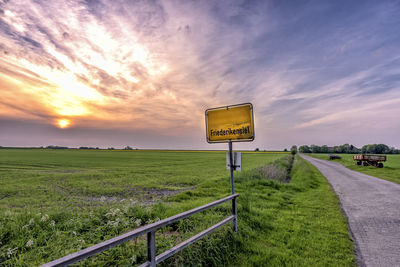 Information sign by grassy landscape at roadside during sunset