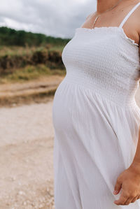 Midsection of pregnant woman in white dress