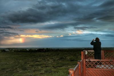 Rear view of man photographing sea against sunset sky