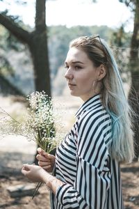 Side view of young woman standing against plants