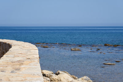An old ancient wall with clear blue sky and blurred sea in the background in chania