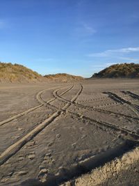 Tire tracks on desert road against sky