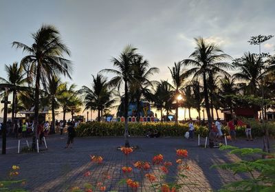 People in park by palm trees against sky