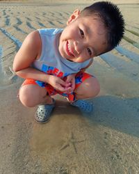 Portrait of cute boy crouching on sand at beach