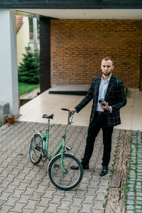 Portrait of man with bicycle standing against wall