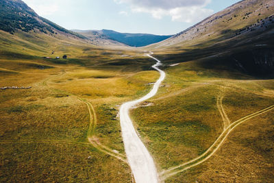 Aerial drone view of paved gravel mountain road in the center of a valley at high altitude.