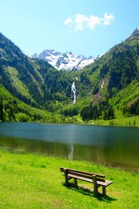 Bench in park by lake against sky