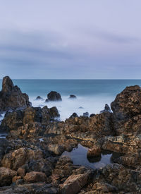 Scenic view of rocks at sea shore against cloudy sky