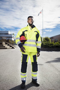 Full length portrait of confident auto mechanic student wearing reflective jacket outdoors