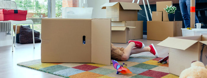 Low section of boy in cardboard box on carpet at home