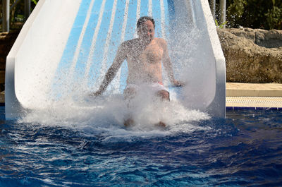 Full length of shirtless man enjoying on slide at water park