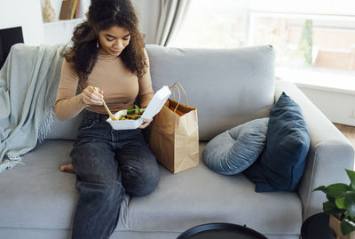 Young woman using digital tablet while sitting on sofa at home