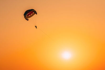 Low angle view of person paragliding against orange background