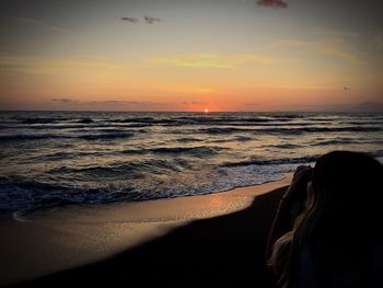 Rear view of woman standing on beach against sky during sunset