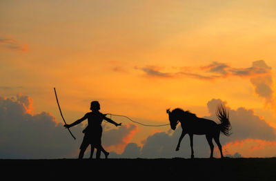 Silhouette people with horse on field against sky during sunset