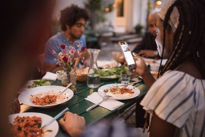 Young woman using mobile phone while having dinner with friends during garden party