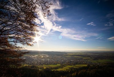 Sunlight streaming through trees on landscape against sky