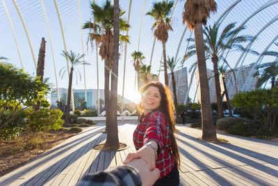 Portrait of young woman standing against palm trees