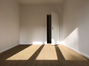 Sunlight falling on empty apartment room, white painted walls and brown carpet