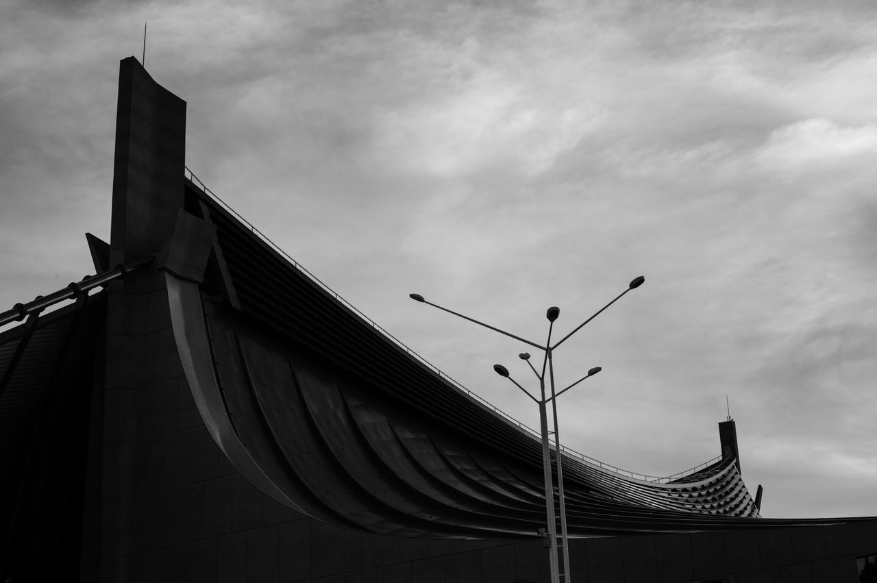 low angle view, architecture, built structure, building exterior, sky, cloud - sky, high section, cloud, cloudy, roof, building, outdoors, no people, day, railing, city, overcast, bird, street light, house