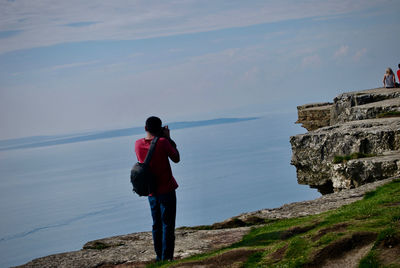 Rear view of man standing on rock by sea against sky