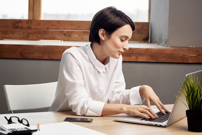 Woman using laptop while sitting by table