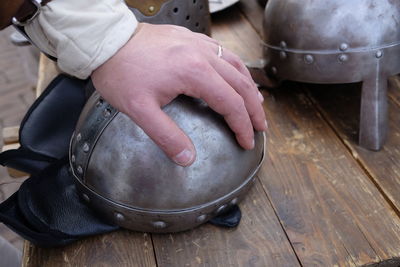 Cropped hand of man touching traditional helmet on wooden table