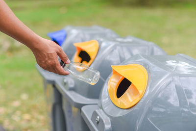 Close-up of hand putting bottles in recycling bin
