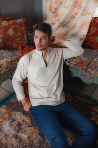 Young mixed race man sitting on old rug near vintage sofa at home
