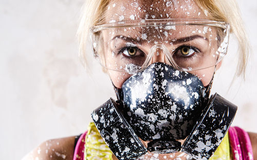 Portrait of female construction worker wearing stained protective mask against wall