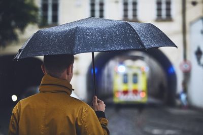 Rear view of man with umbrella on wet street