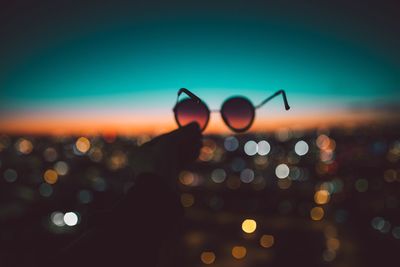 Cropped image of hand holding sunglasses against illuminated city