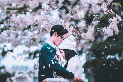 Side view of young couple embracing by flowering tree