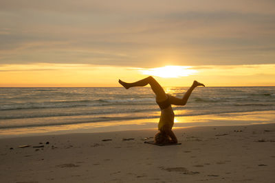 Woman doing yoga in sea against sky during sunset