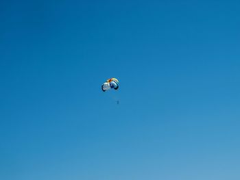 Low angle view of parachute flying in clear blue sky