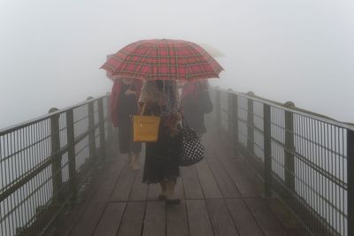 Women with umbrellas walking on footbridge during foggy weather