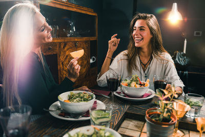 Cheerful female friends eating food at table in restaurant
