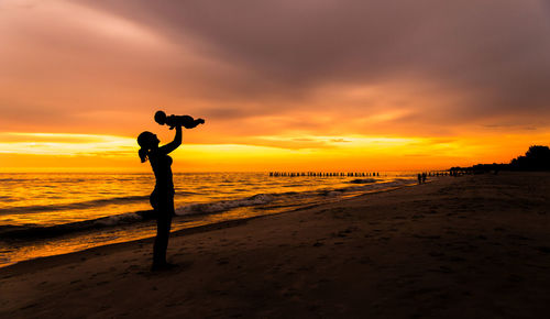 Silhouette woman standing at beach against sky during sunset