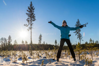 Full length of woman jumping on snow during sunny day