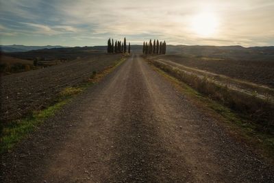 Dirt road amidst field against sky